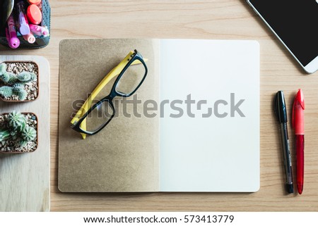 Blank notebook over wooden table with a pen, smartphone, yellow glasses.