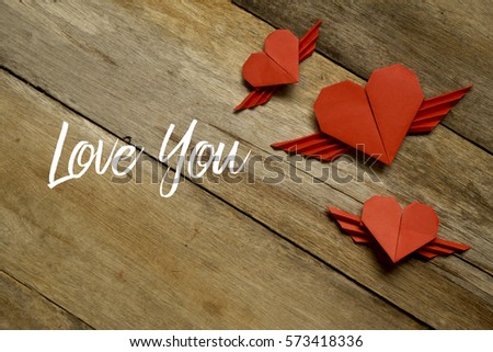 Valentine concept. Red paper origami heart with wings with LOVE YOU written on wooden background.
