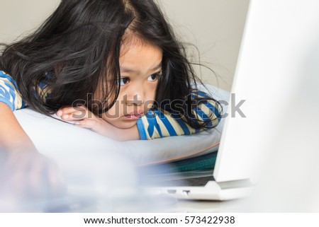 Baby lay on the bed and looking the cartoon movie in computer laptop in living room
