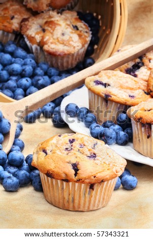 Delicious homemade blueberry muffins with fresh blueberries spilling from a wooden spoon and wicker basket.