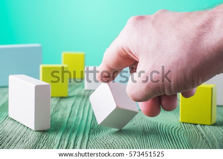 Hand holding wooden cube element. The concept of logical thinking. Geometric shapes on a wooden background. Man's hand holding wooden block. Colorful wooden blocks.