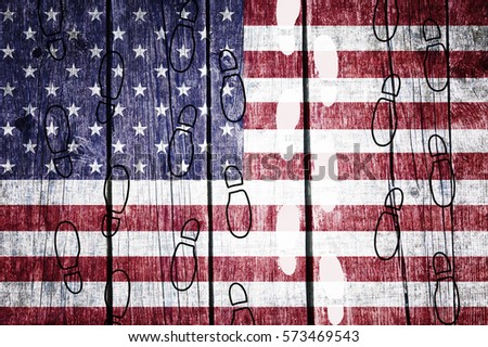 White shoeprints among black ones on a aged wooden background with painted Usa flag shows otherness, orientations, etc.