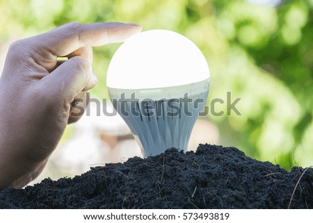 growing light bulb from soil with hand touching on nature art abstract background. Save energy concept 