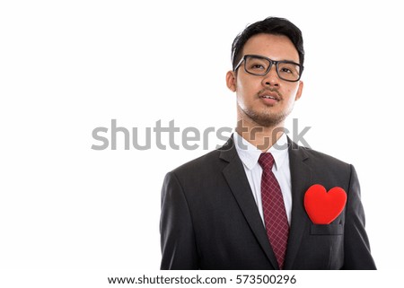 Studio shot of young Asian businessman thinking with red heart on chest