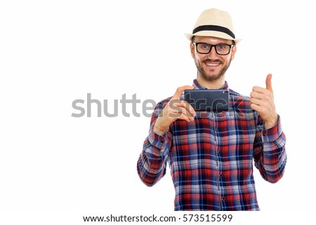 Studio shot of happy young man smiling while taking picture with mobile phone and giving thumb up