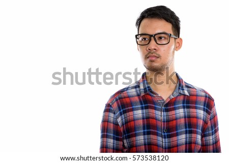 Studio shot of young Asian man thinking and looking at distance while wearing eyeglasses
