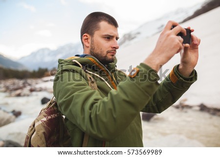 young hipster man, taking pictures using smartphone, wild nature, winter vacation, hiking, traveling, backpacker, warm clothes
