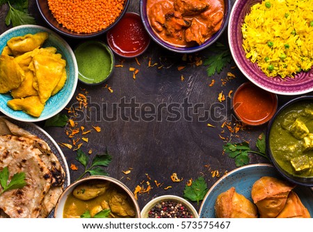 Assorted indian food on dark wooden background. Dishes of indian cuisine. Curry, butter chicken, rice, lentils, paneer, samosa, naan, chutney, spices. Space for text. Bowls and plates with indian food Royalty-Free Stock Photo #573575467