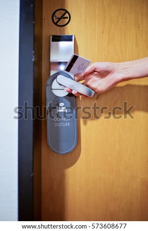 Female hand opening a hotel room door with a sign do not disturb and no smoking