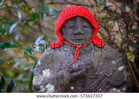 Close-up detail of a stone Jizo Bosatsu statue with a red knitted woollen cap. Travel and religion concept.