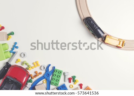 Colorful kids toys: plastic toy tools, nuts, bolts, car, train, cubes, bricks with wooden rail on white background as frame with copy space for text. Flat lay. Top view. Toned picture