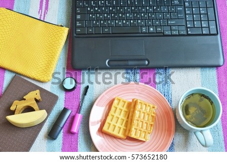 Women working place at home. Keyboard computer, notebook, toy wooden horse, a cup of green tea, waffles, cosmetics and yellow cosmetic bag on a purple striped rug. Lunch break beauty blogger. Flay lay