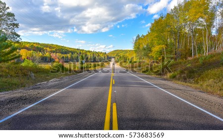 Sunny road to anywhere, single point perspective down a country highway in summer.  Warm day to drive or travel to anywhere. Royalty-Free Stock Photo #573683569