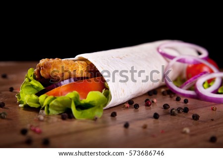 Chicken roll with lettuce tomato onion and pepper on a wooden table and black background.