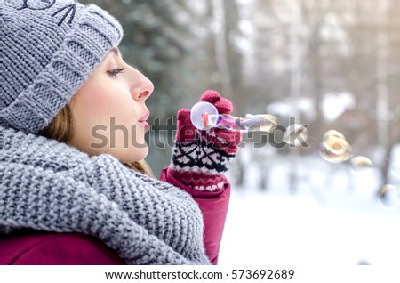 Young beautiful woman blowing bubbles  in winter clothing outdoors. Focus on lips. Soap bubbles.