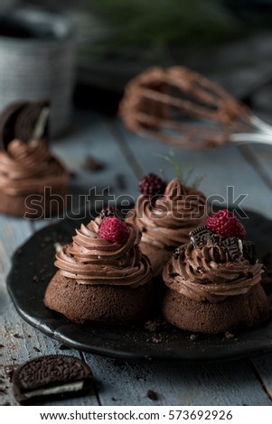 Three chocolate cakes on black plate. Half of a dark brown biscuit ,whisk and another cake out of focus standing on wooden rustic light blue table.