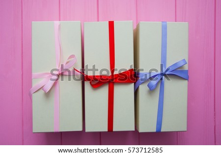 Cute gift boxes on pink background top view. Cute Gift boxes with cute bow. Gift boxes with colorful ribbons on wooden pink background. Greeting card for Mother's Day. Beautiful birthday invitation. 