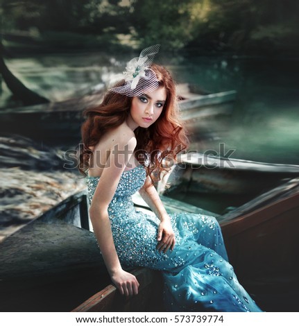 Portrait of a young redhead woman with long curly hair. beautiful bright makeup. turquoise background, this side of the river and trees. girl sitting on the edge of wooden boats.
