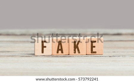 Word Fake on four blank wood cube dices on aged table.