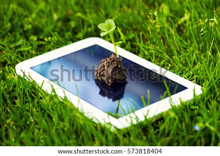 a touch screen of smartphone,tablet,cell phone with seedling growing up on screen over green grass. abstract background to green communication technology concept.