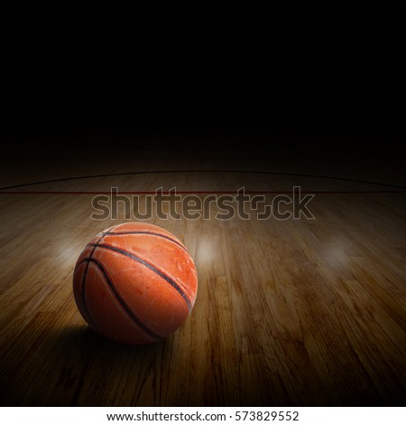 Dramatic spot lighting on basketball arena with rugged and seasoned ball on court and copy space.