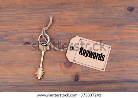 Key and a note on a wooden table with text: Keywords
