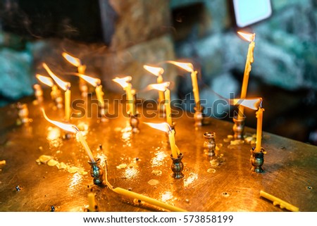 Small wax candles stuck in a tray burn outdoors at blowing wind. Orthodox Christianity religious tradition to set flaming candles while worshiping God