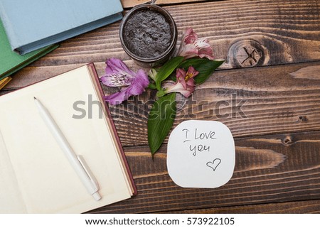 Notepad, flowers and scrub on a wooden table. Note "I love you"