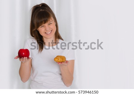 Girl in a white T-shirt holding a croissant and an apple. Harmful and wholesome food. Woman with food
