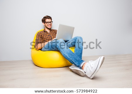 Happy young man sitting in yellow pouf  and using laptop.