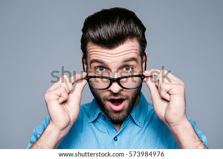 Wow! Surprised young man with opened mouth touching glasses. Royalty-Free Stock Photo #573984976