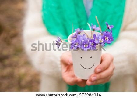 Woman holding beautiful snowdrops in a paper cup. first spring flowers in a forest. Wild flowers. spring concept.