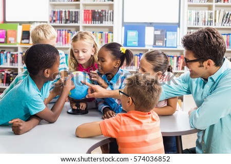 Teacher and kids discussing globe in library at school Royalty-Free Stock Photo #574036852