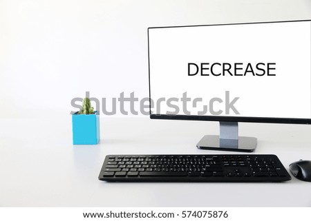 Computer screen on wooden desk with text DECREASE in modern office.
