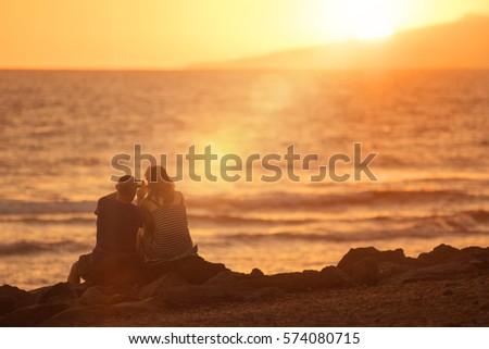 Couple in love taking pictures on the beach at sunset. Lens flare effect.