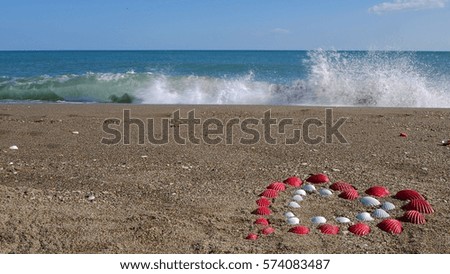 Two hearts in the sand of the sea against the backdrop of the waves. Red and white heart. Two hearts made of shells on the sea sand. The explosion of spray from the waves. Beautiful wave.