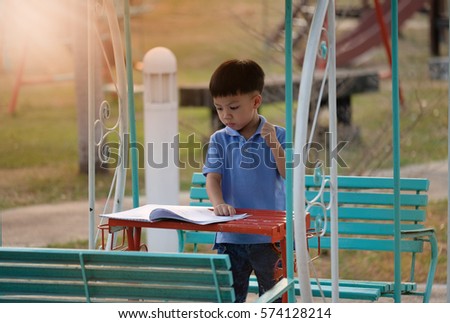 A cute boy standing on bench in the park in a fine sunny afternoon, reading a book and educating themselves preparing for the examination