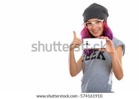 Studio shot of happy geek girl smiling while taking picture with mobile phone and giving thumb up
