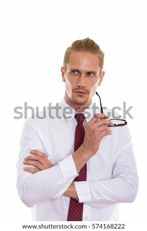 Studio shot of young handsome businessman thinking and looking up while holding eyeglasses