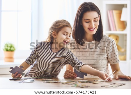 Happy family. Mother and daughter do puzzles together. Adult woman teaches child to solve puzzles. Royalty-Free Stock Photo #574173421