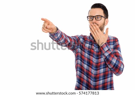 Studio shot of young man pointing at distance while looking shocked
