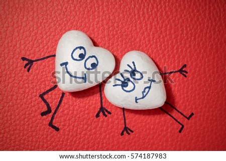 Two white hearts with happy faces on red leather background
