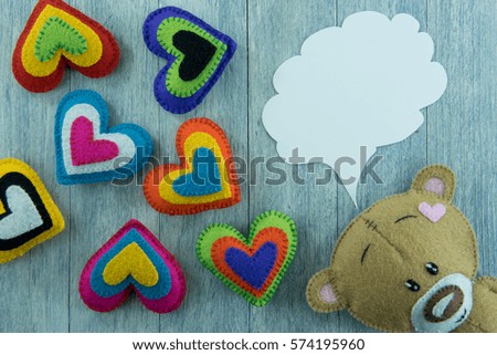 Valentines Day postcard. Teddy Bear and colourful hearts and free space for greetings in speech bubble on a wooden background.