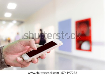 Man use mobile phone, blur image of walkway in hospital near the emergency door and fire extinguishers as background.