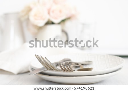 Vintage silverware set on plates against roses bouquet at background. Light pastel colored image. Soft focus, shallow DOF, focus on top of forks.