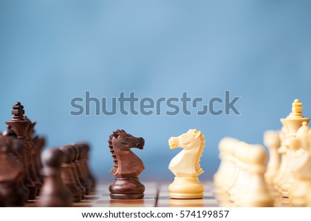 Chess pieces knights facing each other for a standoff on chessboard with blue background. Chess knights confronting each other. Chess knights head to head. 