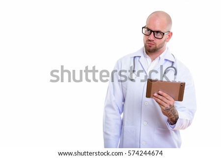 Studio shot of young bald muscular man doctor holding digital tablet while thinking