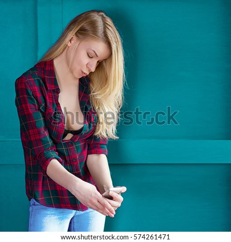 Beautiful girl is doing selfie. Blonde girl in a plaid shirt with a phone. hipster portrait with a smartphone.