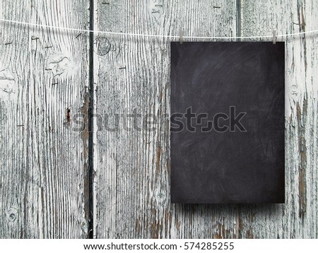 Blank blackboard frame hanged by pegs against gray weathered wooden boards background