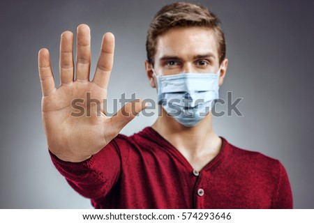 Stop the infection! Healthy man showing gesture "stop". Photo of man wear protective mask against infectious diseases and flu. Health care concept. Royalty-Free Stock Photo #574293646
